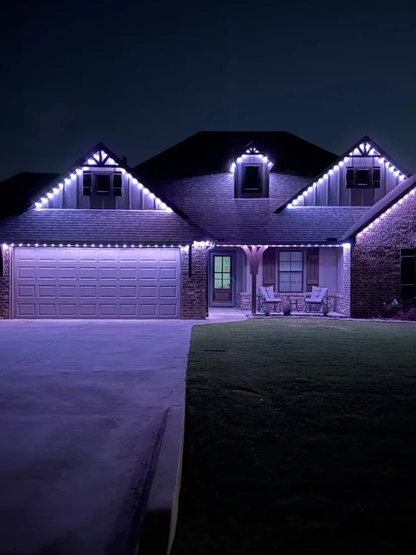 Lakeside home outlined in red and white permanent lighting, seen from above at dusk