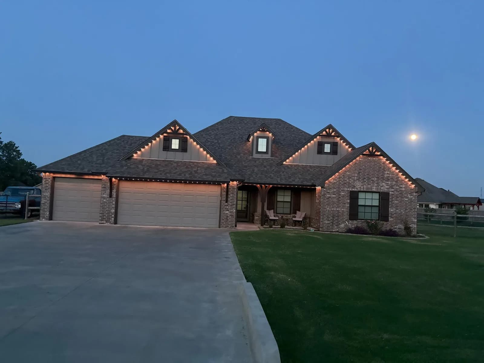 Brick ranch home outlined in purple and white permanent lights at dusk