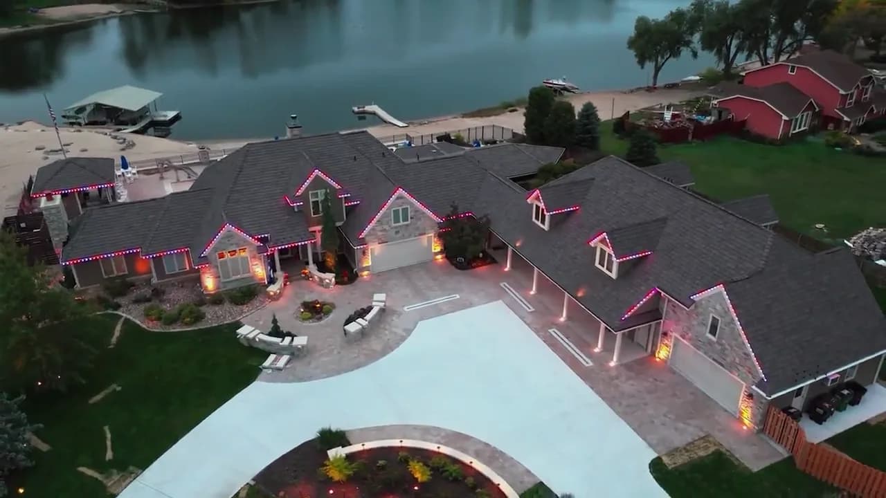 Lakeside home outlined in red and white permanent lighting, seen from above at dusk